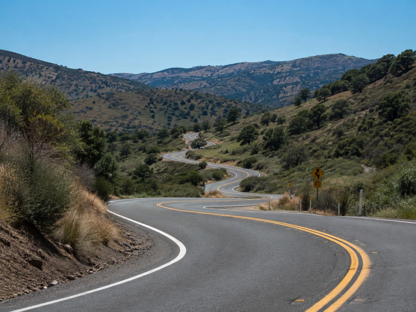 A winding two-lane road descending through dry hills under a clear sky